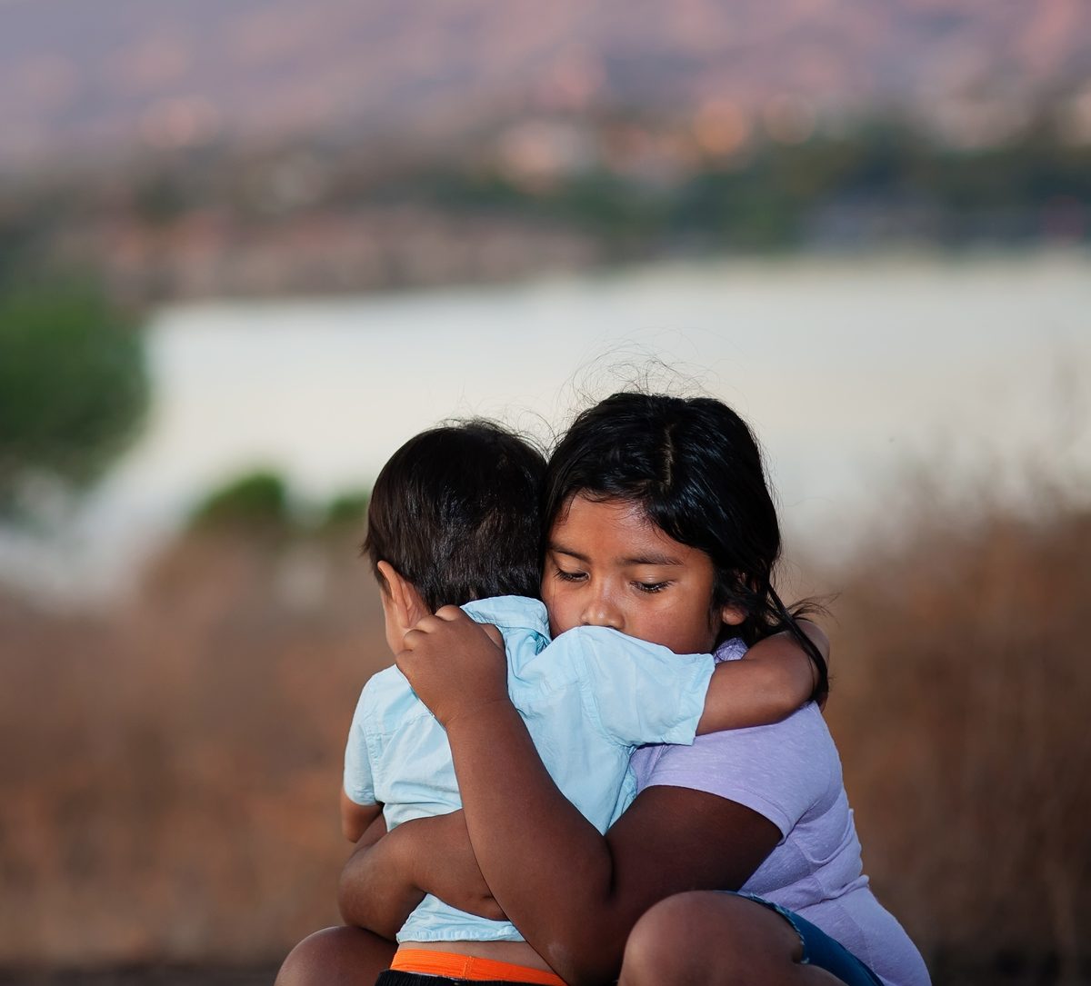 A young girl holding her younger brother in a protective embrace